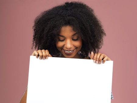 Im happy to present this to you. Studio shot of an attractive young woman holding a blank placard against a pink background.の写真素材
