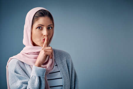 This is our little secret. Studio shot of an attractive young woman standing with her finger on her lips against a grey background.の写真素材