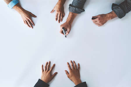 Business people writing on white paper in meeting, planning a marketing strategy and writing creative ideas together from above. Top view of hands of team of designers drawing a design on blank pageの写真素材