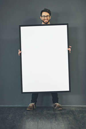 Man standing with a blank sign or portrait frame, showing copy space for advertising or marketing with dark background. Happy, smiling and intelligent guy holding big white poster or page copyspaceの写真素材