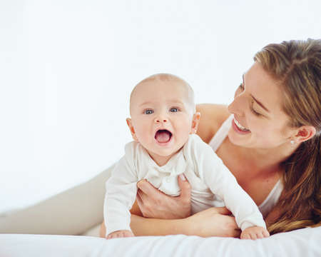 Loving mother and baby bonding at home, playing while relaxing on a bed together. Happy parent being...