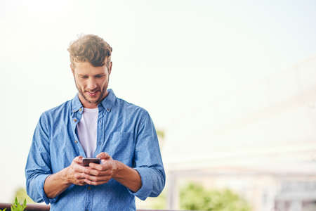 Making plans for the weekend. a confident young man texting on his cellphone outside during the day.