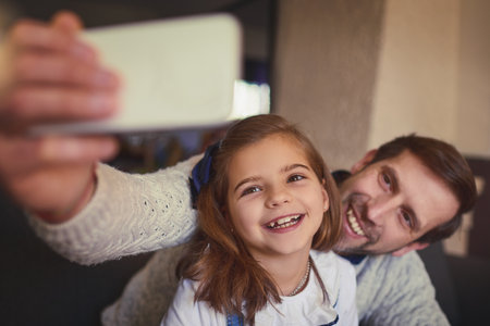 Spending some quality time with his daughter. a handsome man and his adorable young daughter taking selfies on the sofa at home.の写真素材