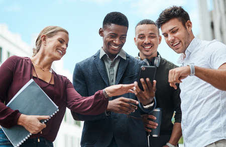 Young, diverse and creative design team and their manager looking at phone together outside from...