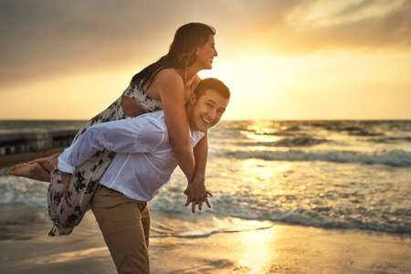 Cropped portrait of a handsome young man piggybacking his girlfriend on the beach.の写真素材