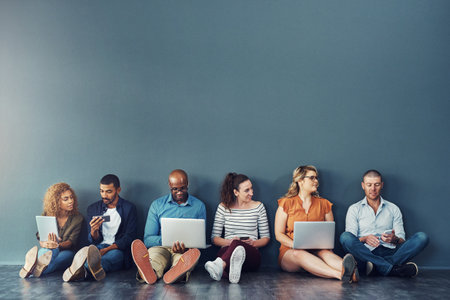 Diverse digital team exploring online platform on many devices, sitting against copy space together. Social advertising and global networking, collaborating with technology, connecting global networkの写真素材