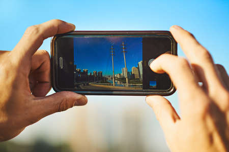 Landscapes are my favorite to capture. an unrecognizable man taking a photo of the city with his cellphone outside.の写真素材