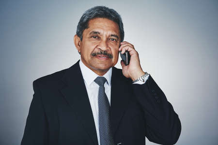 Never keep opportunity waiting on the line. Studio portrait of a mature businessman talking on a cellphone against a grey background.の写真素材