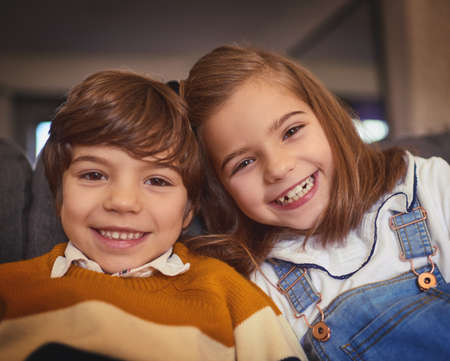 The bond between brother and sister. Cropped portrait of an adorable little boy and his older sister sitting on the sofa at home.の写真素材