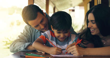 Kids have a way of reminding you of childhood. a young family colouring in together by the table outside.の写真素材