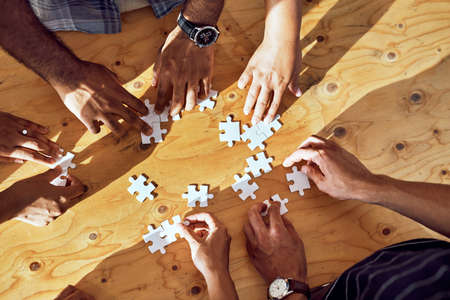 Synergy forms the solutions we need. Closeup shot of an unrecognizable group of people completing a puzzle together.の写真素材