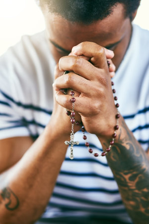 He hears all your prayers. a young man holding his rosary while praying.の写真素材
