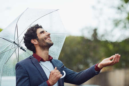 This rain is just what we needed. a handsome young businessman on his morning commute in the rain.