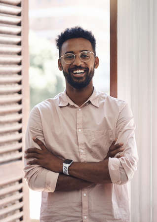 Happy, carefree and positive young business man standing arms crossed in his office at work....