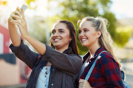 We take photos to look back at our experiences. two beautiful female friends taking a selfie in the city.の写真素材