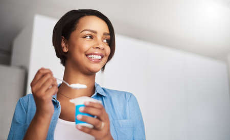 So tasty I could eat it all day. an attractive young woman eating a tub of yoghurt at home.の写真素材