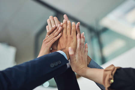 With teamwork, anything is possible. Closeup of a group of unrecognizable businesspeople holding up their hands for a high five in the office during the day.の写真素材