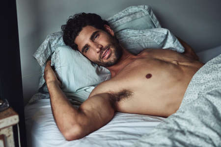 I dont want to get out of bed, it feels too great. a handsome young shirtless man lying in bed at home.の写真素材