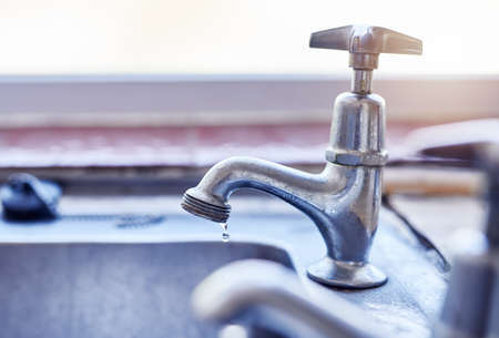 Never leave a tap dripping. two dripping taps waisting a little bit of water in a basin inside of a house during the day.の写真素材