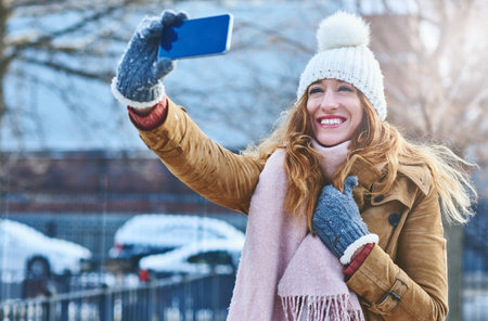 With weather like this I have to take a selfie. an attractive young woman taking a selfie in the snow outside.の写真素材