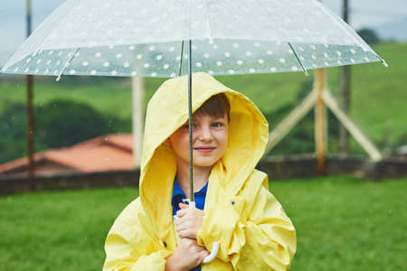 Protected against the weather. Portrait of a cheerful little boy standing with an umbrella outside on a rainy day.の写真素材