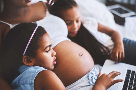 Next movie. two focused little girls relaxing next to their pregnant mother while watching a movie...