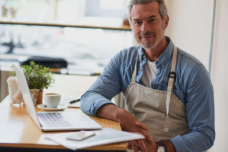 I found success in coffee. Portrait of a handsome mature man doing some paperwork and using a laptop...
