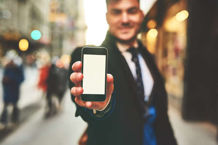 What do you think of this photo. Closeup of a cheerful young man holding up a cellphone and showing...