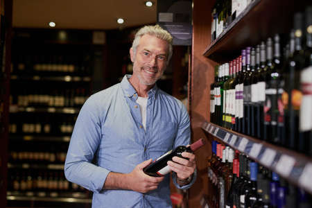 Just the year I was looking for. Portrait of a handsome mature man buying wine at a grocery store.