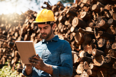 Keeping his eye on the lumber shipments. a lumberjack using his tablet while standing in front of a...