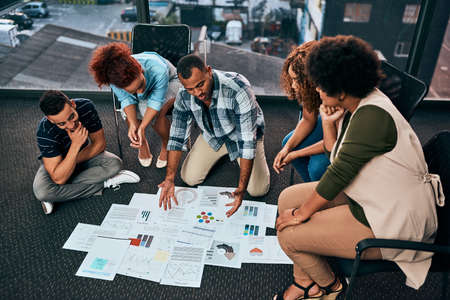 Explaining in detail. a group of focussed young coworkers working together and brainstorming while being seated on the floor of the office at work during the day.の写真素材