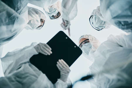 Hazmat healthcare workers from below, working together during pandemic wearing face masks. Team of doctors wearing quarantine suits discussing medical lab results of the virus spreadの写真素材