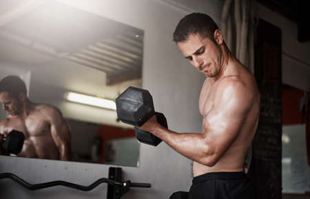 Form equals brawn. a handsome and muscular young man working out with a dumbbell in the gym.の写真素材