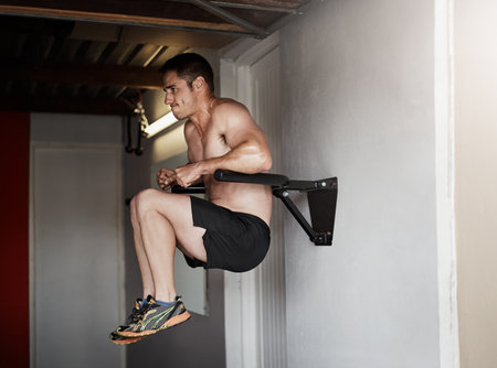 Working on his core. Full length shot of a handsome and muscular young man working out on a dip bar...