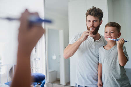 Giving their teeth a good clean. a father and his little son brushing their teeth together in the bathroom at home.の写真素材