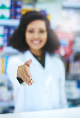 Hello, Im here to help. a young woman extending her arm for a handshake at the counter of a pharmacy.の写真素材