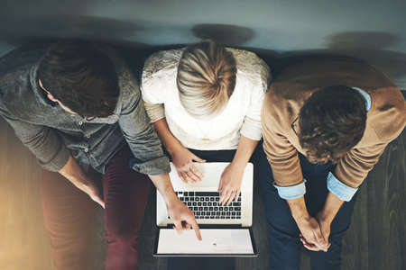 A group of planning, researching and professional business people working together on a laptop while...