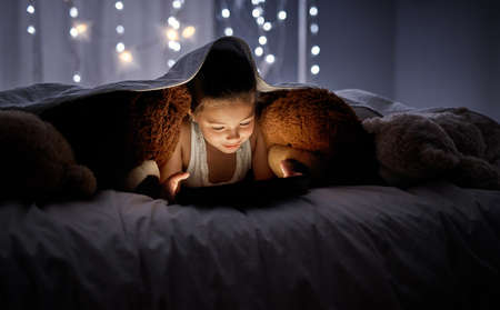 She wants to see the digital world before dreamland. an adorable little girl using a digital tablet in bed at night.の写真素材