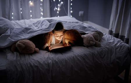 Shes not ready to switch all the lights off just yet. an adorable little girl using a digital tablet...