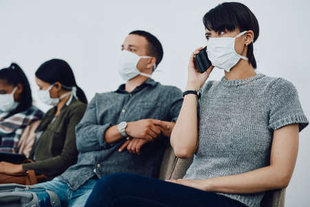 Woman calling while traveling with covid and waiting in line at airport while wearing a mask for protection. For hygiene and healthcare security, follow coronavirus social distance regulationsの写真素材