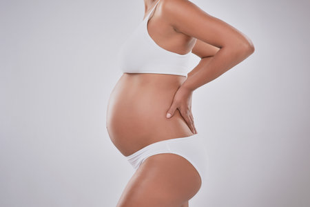 Growing and looking great. Cropped studio shot of a pregnant woman wearing wearing underwear against a gray background.の写真素材