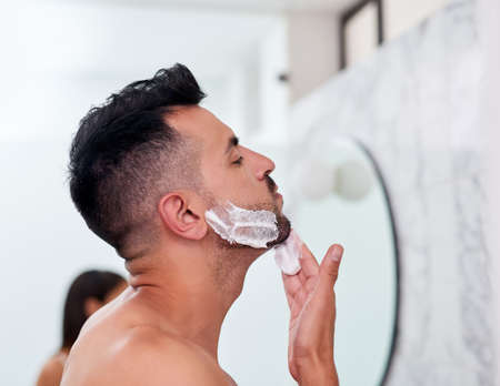 Its all coming off. a handsome young man applying shaving cream to his face in the bathroom.の写真素材