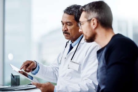 You see this is what my reports are telling me. a confident mature male doctor seated at his desk while consulting a patient inside a hospital during the day.の写真素材