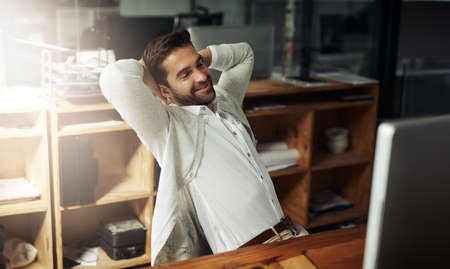 Kicking back after a long but successful day. a handsome young businessman taking a break while working late in an office.の写真素材
