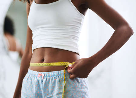 Knocking off the inches. Closeup shot of an unrecognizable woman measuring her waist.
