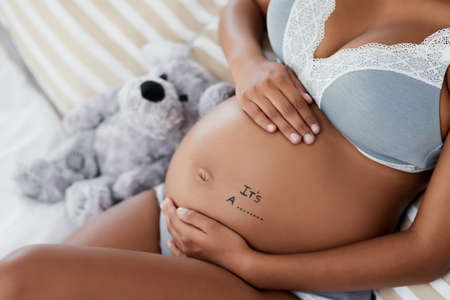 Is it a boy or a girl. High angle shot of a pregnant young woman relaxing on her bed at home.の写真素材
