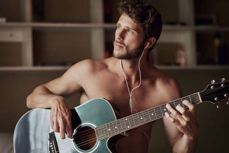 Theres nothing like some music in the morning. a handsome young man playing a guitar at home.