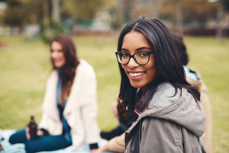 Spending the day just relaxing with good friends. Portrait of a cheerful young woman seated with his friends at a picnic outside during the day.の写真素材