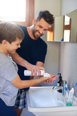 Let me show you how its done. a father squeezing shaving cream into his sons hands in the bathroom.の写真素材