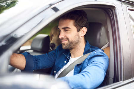 Time spent with pets is never time wasted. a handsome young man sitting in the car with his golden...